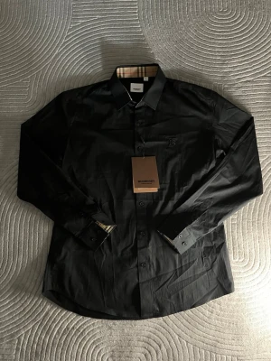 Burberry skjorta - Tjenare! Säljer en burberry skjorta som aldrig använts eftersom den var lite för liten på mig som är runt 185cm 75kg. Den är i perfekt skick och i bästa kvalité. Både kragen och längst ut på ärmarna har lite hårdare material i sig så dem alltid sitter på plats. Lapp finns kvar på och den har det klassiska rutiga mönster inne i kragen och längst ut i ärmarna vilket gör den sticker ut lite extra när du har vikit upp dem. Perfekt för dig som vill vara lite extra stilig och sticka ut bland andra 👔💎