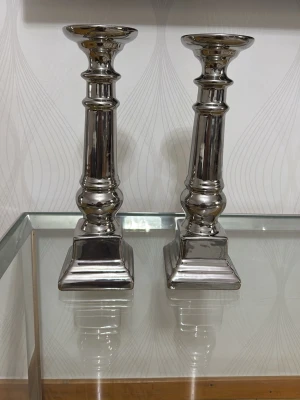 Två silverfärgade ljusstakar i metall - Säljer ett par stilrena ljusstakar i silverfärgad metall med klassisk design och fyrkantig fot. Perfekta som dekoration på bord eller hylla. Passar vanliga stearinljus och ger ett elegant intryck i rummet.