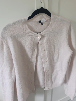 Ljusrosa kofta med rund hals - *den e mer rosa i verklighet men ljuset tar inte upp det* Mysig ljusrosa kofta med rund halsringning och knappar framtill. Koftan är stickad i ett mjukt material och har långa ärmar samt ribbade muddar vid hals, ärmslut och nederkant. Perfekt att slänga över en topp för en chill look.