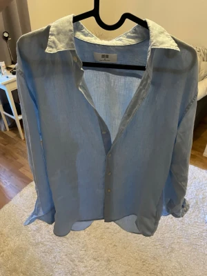 Ljusblå linneskjorta från Uniqlo - Snygg och luftig ljusblå skjorta från Uniqlo i linne. Skjortan har klassisk krage, knäppning framtill och långa ärmar. Perfekt för en avslappnad och stilren look.