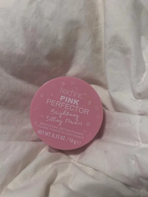 Technic Pink Perfector Setting Powder - Technic Pink Perfector Brightening Setting Powder i en rund burk med rosa lock. Pudret är ljust och används för att fixera makeup och ge en uppljusande effekt. Perfekt för att få en fräsch finish på din bas. Innehåller 10 g. Har använt en gång.