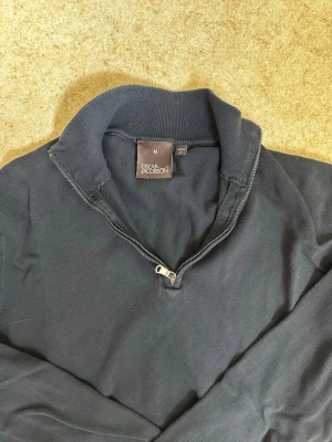 Mörkblå halvzip-tröja Oscar Jacobson - Mörkblå  långärmad tröja från Oscar Jacobson med halvzip och ståkrage. Tröjan har ribbade muddar vid ärmslut och nederkant. Perfekt för en stilren och avslappnad look. Säljs för 200kr. Kontakta mig om du har frågor eller vi lägga bud.