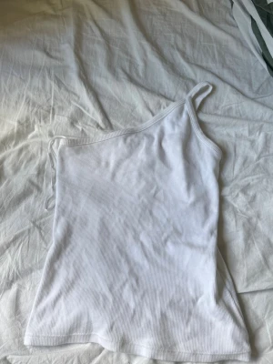 Vit oneshoulder ribbad topp - Säljer en vit ribbad topp med oneshoulder-design och smalt axelband. Materialet är mjukt och stretchigt, den är super bekväm.