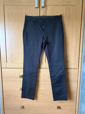 Svarta chinos med rak passform - Snygga svarta chinos från MQ:s  med rak passform och klassiska fickor fram och bak. Byxorna har bälteshällor och stängs med knapp och dragkedja. Tillverkade i ett mjukt bomullsmaterial som ger en clean och stilren look.