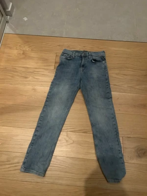 Ljusblå raka jeans  - Säljer ett par ljusblå jeans med rak passform och klassisk femficksdesign. Jeansen har normal midja och stängs med knapp och dragkedja. Tillverkade i denim med en tvättad look som ger en avslappnad stil.