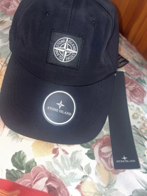 Svart keps från Stone Island - Snygg svart keps från Stone Island med klassisk kompasslogga framtill. Justerbar baktill och tillverkad i ett slitstarkt material som andas. Perfekt accessoar för en streetwear-look och passar till det mesta.