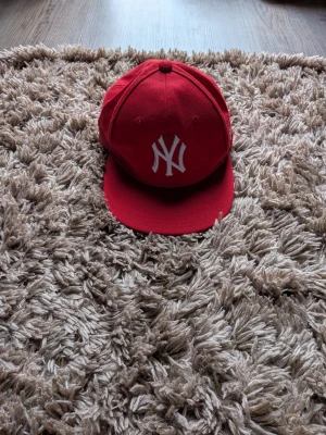 Röd New York Yankees keps - Snygg röd keps med klassiskt New York Yankees-logga broderad i vitt framtill. Kepsen har en rak skärm och  Perfekt accessoar för att lyfta din streetwear-look.