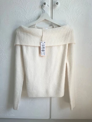 Offshoulder vit stickad tröja Gina Tricot - Supersnygg offshoulder stickad tröja från Gina Tricot i krämvit färg. Tröjan har bred ribbad kant upptill och långa ärmar. Mjuk och fluffig känsla, perfekt för kalla dagar. Enkel att styla med jeans eller kjol.