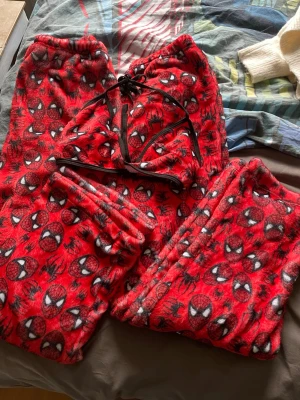 Röd Spiderman pyjamas-set - Matchande spiderman pyjamas sett. Det är en killmodell och en tjejmodell killmodellen är lite längre än tjejens och mått delas ut på begäran. Det helt nya och perfekt för som gåva till sin pojkvän/flickvän. Det ingår även en bikini liknande topp med samma tryck. Materialet är fluffigt och mjukt, perfekt för chillkvällar hemma.