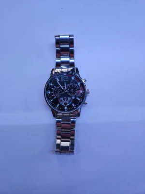 Stilren silverfärgad klocka - Snygg klocka med metallarmband i silver och svart urtavla med flera detaljerade visare och markeringar. Klockan har en klassisk rund form och robust känsla, perfekt för dig som gillar stilrena accessoarer med lite edge. Priset kan diskuteras