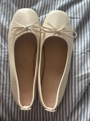 Vita ballerinaskor med rosett - Säljer ett par stilrena vita ballerinaskor med fyrkantig tå och söt rosettdetalj framtill. Skorna har en slät ovandel i konstläder och mjuk innersula för extra komfort. Passar perfekt till jeans eller klänning för en clean look.