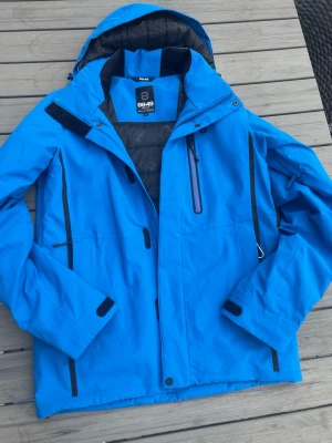 Blå skidjacka med huva från 8848 Altitude - Snygg blå skidjacka från 8848 Altitude med svart foder och detaljer. Jackan har flera dragkedjeförsedda fickor, justerbar huva och kardborre vid ärmsluten. Perfekt för kalla dagar och outdoor-aktiviteter. Den är oanvänd och nypris är ca 2700. Hör av dig vid frågor!