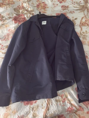 Mörkblå overshirt från John Henric - Stilren mörkblå overshirt från John Henric med klassisk krage, knappstängning och två bröstfickor med lock. Tillverkad i ett slätt tyg som ger en clean look. Perfekt att bära över en t-shirt för en avslappnad men snygg stil.