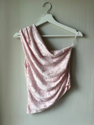 Ljusrosa spets one shoulder topp - Säljer en ljusrosa asymmetrisk topp med ett axelband och vacker spetsdetalj. Toppen har en draperad passform och är perfekt för dig som gillar unika snitt och romantisk stil. Materialet är mjukt och har ett blommigt mönster i spets. Den har aldrig använts och prislappen är kvar. Jag kunde inte hitta den på hemsidan men nypriset på liknande toppar ligger runt 300-350kr.💕