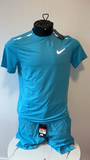 Blått träningsset från Nike - Säljer ett fräscht blått träningsset från Nike med matchande t-shirt och shorts. Setet har en sportig look med korta ärmar och Nike-logga på bröstet. Perfekt för gymmet eller löprundan. Materialet är lätt och andas bra.