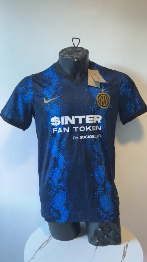 Blå Inter Milan matchtröja Nike - Snygg blå och svart Inter Milan matchtröja från Nike med guldfärgade detaljer och klubbmärke på bröstet. Tröjan har korta ärmar, rund hals och ett unikt mönster i blå toner. Tillverkad i lätt och ventilerande material, perfekt för fotbollsträning eller match.