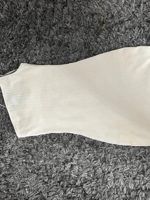 Vit ribbad ärmlös långklänning - Säljer en stilren vit långklänning med ribbad struktur. Klänningen är ärmlös och har en enkel, figurnära passform som ger en clean och modern look. Perfekt för dig som gillar minimalistisk stil.