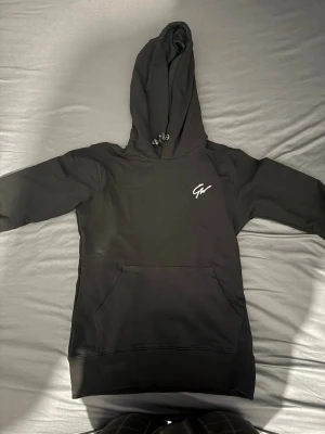 Svart hoodie från Gorilla Wear - Säljer en svart hoodie från Gorilla Wear med vit logga på bröstet och tryck på ryggen. Hoodien har stor huva med dragsko och en klassisk magficka. Perfekt för dig som gillar streetwear och vill ha en stilren look.