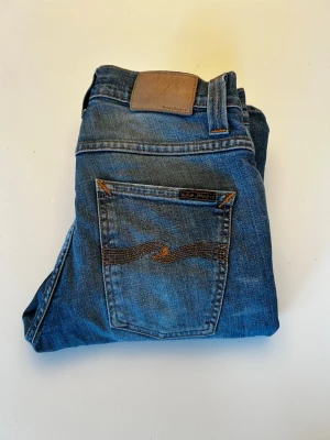 Blå jeans från Nudie Jeans - Säljer ett par klassiska blå jeans från Nudie Jeans i modellen Grim Tim. Strl: 28/32 Skriv innan köp. Pris: 399 OBS! Litet hål i grenen‼️