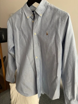 Ralph Lauren skjorta  - Klassisk ljusblå oxfordskjorta med button-down krage och vita knappar. Skjortan har lång ärm och en liten broderad logga på bröstet. Perfekt till jeans eller chinos för en clean och stilren look. Storlek 14-16 men passar S. Pris kan diskuteras 🙌🏻💯