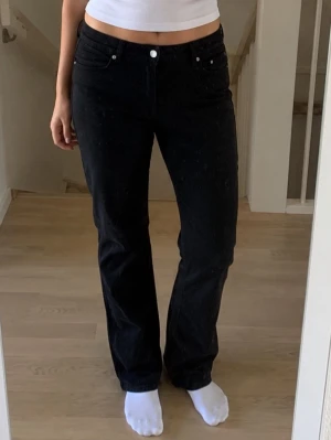 Svarta raka jeans med hög midja - Snygga svarta jeans med rak passform och hög midja. Klassisk femficksmodell med knapp och dragkedja framtill. Perfekta till en enkel topp eller hoodie för en clean look.