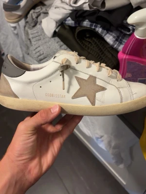 Golden Goose  - Snygga vita sneakers med beige mockadetaljer och en stor stjärna på sidan. Skorna har beige snören och en något smutsad sula för en avslappnad look. Tillverkade i läder och mocka, perfekt för dig som gillar streetstyle.