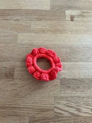 Virkad röd scrunchie - En blå scrunchie i mjukt garn med volangkant. Perfekt för att sätta upp håret eller ha som accessoar runt handleden. Färgen är röd och materialet känns lent och följsamt.