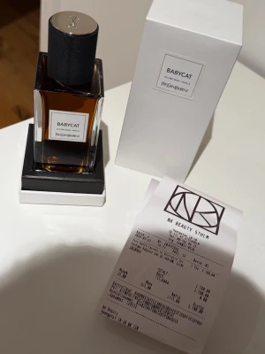 Yves Saint Laurent Babycat parfym - Exklusiv parfym från Yves Saint Laurent med namnet Babycat. Flaskan är rektangulär i klart glas med svart cylinderformad kork och etikett framtill. Doften har inslag av vanilj och eleganta noter. Kommer i stilren vit förpackning. Tillkommer med kvitto 