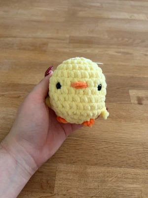 Virkad kyckling - Säljer en liten, rund och mjuk virkad kyckling i ljusgul färg med orange näbb och fötter samt svarta ögon. Perfekt som dekoration eller present. Tillverkad i garn med struktur som ger ett fluffigt intryck.