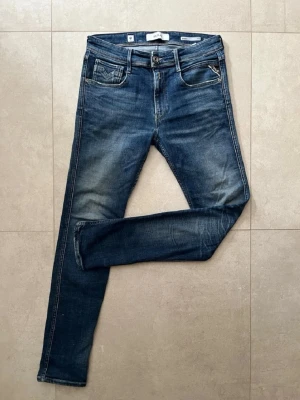 Replay jeans - Snygga blå slim fit jeans med lätt slitna detaljer och klassisk femficksdesign. Jeansen har en skinnpatch bak i midjan och kontrastsömmar. Perfekta för dig som gillar en avslappnad men trendig look.
