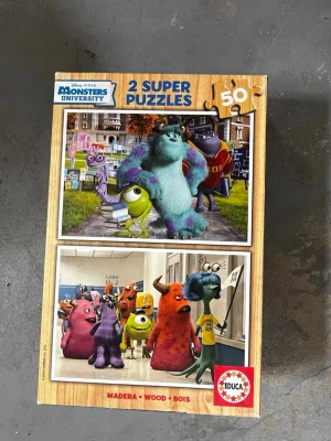 Monsters University 2-pack pussel - Säljer ett 2-pack pussel med motiv från Disney Pixar Monsters University. Varje pussel har 50 bitar och visar färgglada karaktärer som Sulley och Mike. Pusselbitarna är av trä och förpackningen är dekorerad med bilder från filmen.