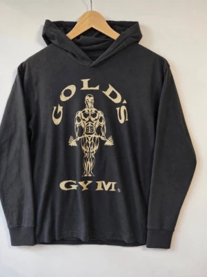 Golds Gym Hoodie - Storlek: S Mått: Armhåla till armhåla: ca 49 cm Längd: ca 65 cm Skick: Mycket fint skick enligt bilder. Inget att anmärka på. En riktigt bra Gold's Gym-hoodie för den som gillar klassisk bodybuilding, gymwear och lite mer retro/vintage träningsstil.  Detaljer: Gold's Gym original/licensierad produkt Modell/artikel: GGTOP-009 80 % bomull / 20 % polyester Mörk antracitgrå Beige/offwhite distressed fronttryck Huva utan dragsko Lang ärm med ribbade muddar Tillverkad/licensierad av Pan World Brands.