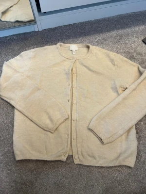 Stickad kofta - Mysig beige kofta från H&M i storlek XS. Koftan har rund halsringning, långa ärmar och knäppning framtill med matchande knappar. Tillverkad i mjukt stickat material som passar perfekt för lager på lager och en clean look.