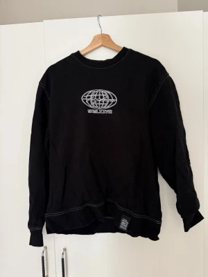 Svart sweatshirt med tryck - Cool svart sweatshirt med vitt tryck av en jordglob och texten MCMLXXVIII på bröstet. På ryggen finns ett större tryck med glob, LDN och signatur. Tröjan har vita kontrastsömmar, rund hals och muddar vid ärmslut och nederkant. Bra skick. Storlek M