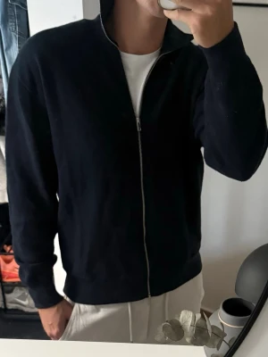 Massimo dutti full zip  - En stilren marinblå ziptröja med hög krage och hel dragkedja framtill från Massimo dutti. Tröjan har långa ärmar och ribbade muddar vid ärmslut och nederkant. Perfekt för lager-på-lager och enkel att matcha med olika outfits. Lite nopprig annars bra skick