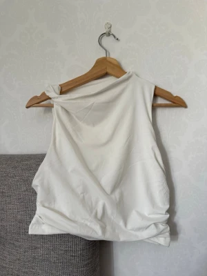 Vit oneshoulder croppad topp - Säljer en vit oneshoulder croppad topp i mjukt material. Toppen är ärmlös och har en asymmetrisk axel, vilket ger en trendig och modern look. Perfekt att styla med höga jeans eller kjol för en cool outfit.