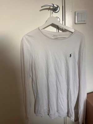 Vit långärmad topp från Polo Ralph Lauren - Klassisk vit långärmad topp från Polo Ralph Lauren med rund halsringning o loggan på bröstet. Perfekt basplagg för alla tillfällen. Ganska stor i storleken. 