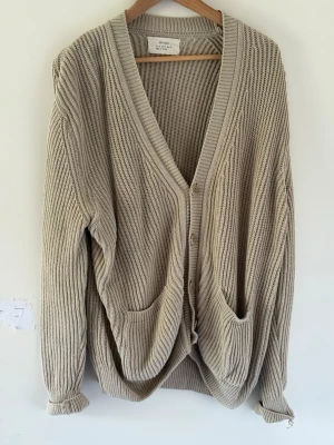 Beige stickad kofta från Zara - Säljer en beige stickad kofta från Zara Origins i storlek M. Koftan har djup V-ringning, knäppning framtill med tre knappar och två stora fickor. Tillverkad i grovstickat material som ger en avslappnad och trendig look.