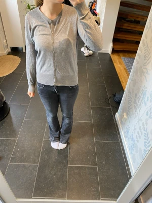Grå basic kofta med knappar - En enkel och stilren grå kofta med rund halsringning och knäppning framtill. Koftan har långa ärmar och ribbade muddar vid ärmslut och nederkant. Perfekt att slänga över en t-shirt eller linne för en avslappnad look.