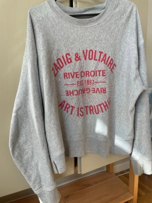 Grå sweatshirt Zadig & Voltaire - Säljer en grå sweatshirt från Zadig & Voltaire med röd text och tryck framtill där det står 'Art is truth', 'Rive Droite' 💕Perfekt för en avslappnad och cool stil. Tröjan är i mycket bra form men några ”diamanter” har ramlat av inget man märker dock !