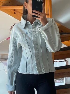 Ljusblå figursydd jeansjacka H&M - Snygg populär ljusblå jeansjacka med figursydd passform från H&M. Jackan har långa ärmar, knäppning framtill med silverfärgade knappar och markerade sömmar. Endast använd ett fåtal timmar