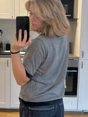 Randig tröja - Säljer en svartvit, smalrandig topp med korta ärmar. Toppen har svarta kontrastkanter vid ärmslut, halsringning och nederkant. Modellen är rak och något loose fit, perfekt till jeans. Materialet känns som bomull eller en mjuk blandning.