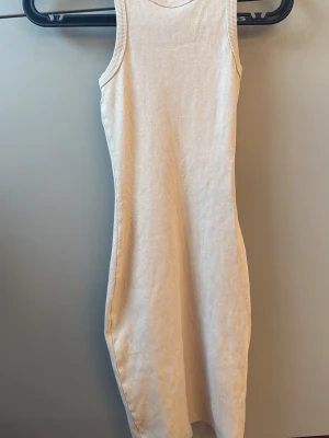 Ribbad ärmlös beige klänning - Snygg ribbad beige klänning i stretchigt material. Modellen är ärmlös och har en kroppsnära passform med rund halsringning. Perfekt för varma dagar eller att styla med en skjorta över.