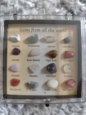 Samling ädelstenar i ask, 16 st - Säljer en samling med 16 olika ädelstenar och kristaller i en genomskinlig ask. Innehåller bland annat howlite, aventurin, citrin, labradorit, ametist, rosenkvarts och tigeröga. Perfekt för dig som gillar stenar, kristaller eller vill börja samla.