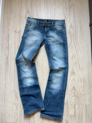 Blå raka jeans med slitningar - Säljer ett par blå jeans med raka ben och snygga slitningar framtill. Jeansen har klassisk femficksdesign, ljusare tvättade partier och detaljerade bakfickor. Perfekta för en avslappnad och trendig look. Super snygga men tyvärr lite för stora för mig. 