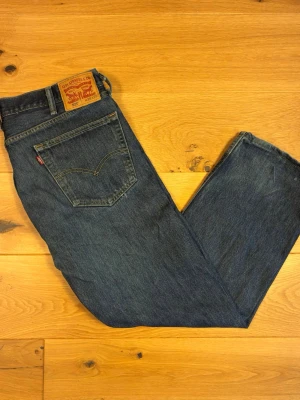 Levi’s 505 W38 L29 - Klassiska Levi’s 505 i mörk/medeltvättad blå denim med naturlig nyansering och fin patina. Rak, avslappnad passform (straight fit) med raka benöppningar – en riktig klassiker som aldrig går ur tiden.  Skick: Fint begagnat skick. Inga hål eller skador som påverkar användningen.  Detaljer:  * Modell: 505, rak passform * Färg: Blå denim, medium/mörk tvätt * Storlek: W38 L29 (enligt innerbrickan) * Äkta läderpatch bak samt röd Levi’s-tab på bakfickan * Knappgylf med kopparnitar * 100% bomull