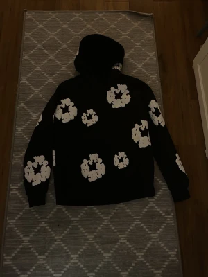 Svart hoodie med vita blommor - Säljer en hoodie från Denmin tears. Hoodien har en klassisk passform med huva och långa ärmar. Perfekt för dig som vill sticka ut med en cool och trendig stil.
