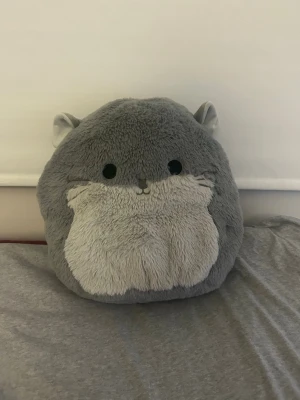 Grå FuzzAMallows Squishmallows gosedjur - Supermjuk och fluffig FuzzAMallows Squishmallows i form av ett runt, grått djur med små öron och ljusare mage. Perfekt som kramkompis eller dekoration i sängen. Tillverkad i plyschmaterial och har söta svarta ögon och liten nos.