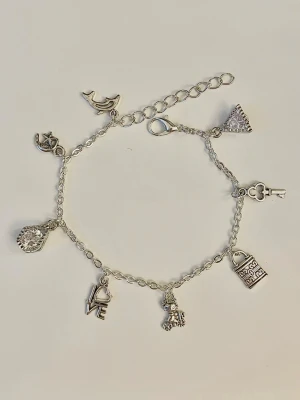 Silverfärgat charmarmband med berlocker - Snyggt handgjordt silverfärgat armband med flera olika berlocker. Kedjan är tunn och har justerbar längd med karbinlås. 21cm lågt och du får armbandet i en gulligt liten tygpåse 