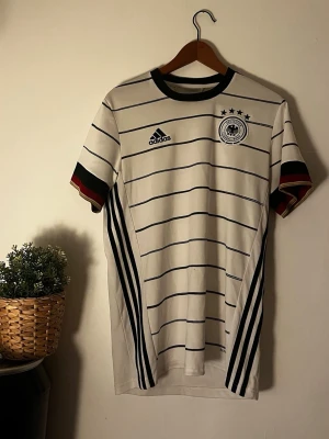 Tysklands matchtröja Adidas vit - Adidas Tyskland fotbollströja 🇩🇪  Snygg Adidas Tyskland-tröja i storlek M. Klassisk vit design med svarta detaljer och Tysklands landslagsmärke.  📏 Storlek: M ✨ Skick: Fint begagnat skick 👕 Passar både till vardags och som fotbollströja.  Säljes då den inte kommer till användning längre.
